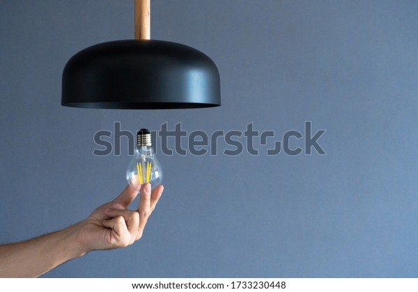 Close-up. A hand changes a\
light bulb in a stylish loft lamp. Spiral filament lamp. Modern\
interior decor