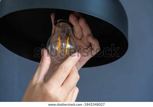 Close-up. A hand changes a\
light bulb in a stylish loft lamp. Spiral filament lamp. Modern\
interior decor
