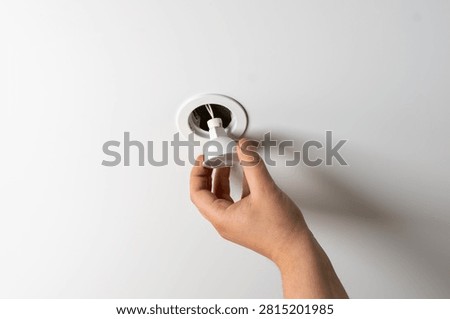 Close-up of a hand changing or installing a white LED spotlight bulb into a recessed ceiling fixture during domestic electrical maintenance and home improvement.