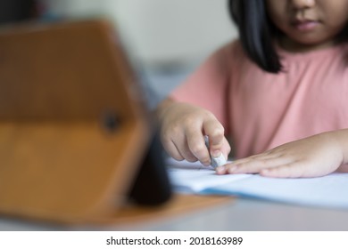 closeup hand of child student back to school or kid girl learning write or draw and using eraser to erase mistaken word on book with smartphone or tablet pad or people learn from home and study online