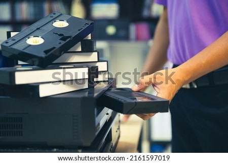 Close-up hand chooses and put or insert video cassette tape VHS old retro style on video record playback concept of vintage electric and electronic appliances multimedia player device old fashioned.