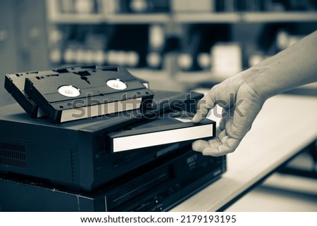 Close-up hand chooses and put or insert video cassette tape VHS on video tape player concept of retro style or vintage electric and electronic appliances multimedia playback device old fashioned.