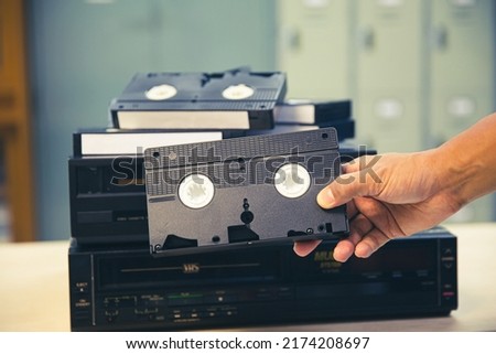 Close-up hand chooses video cassette tape VHS old retro style on video record playback concept of vintage electric and electronic appliances multimedia player device old fashioned.