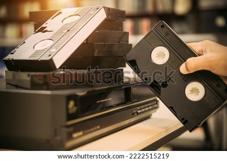Close-up hand chooses video cassette tape VHS on video tape player concept of vintage electric retro style and electronic appliances multimedia player device old fashioned.