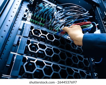 Close-up of a hand connecting network cables in a server rack, showcasing modern technology and data management in an IT environment.