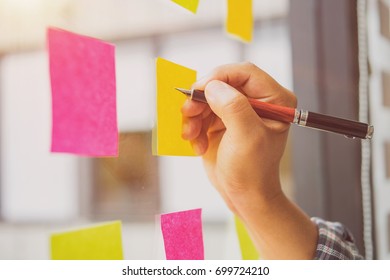 Closeup hand of creative businessman writing on sticky paper at office - Shutterstock ID 699724210