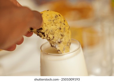 Close-up of a hand dipping a chocolate chip cookie into a glass of milk. - Powered by Shutterstock