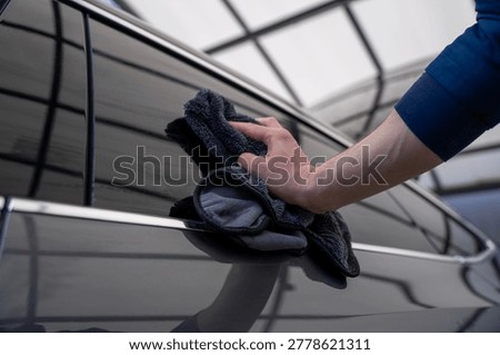 Close-up of hand drying the upper window frame and roof edge of a passenger car with a microfiber cloth after washing.
