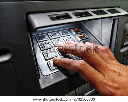 Close-up of a hand entering a PIN code on a silver metallic ATM keypad. Concept of banking security, financial transaction, and cyber safety