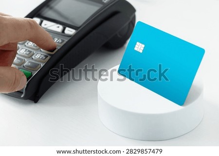 Close-up of a hand entering a PIN code on a payment terminal keypad next to a blue credit card on a stand, representing secure banking transactions and POS retail checkout.