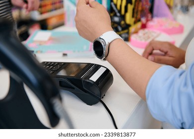 Close-up hand of a female customer using smart watch, making contactless payment using NFC technology, standing by counter in a store with barcode scanner and credit card reader. Business and Finance