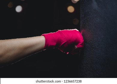 Close-up Of Hand In Fist Pink Protective Insulating Bandage Hits Punching Bag On Black Background. Concept Boxing