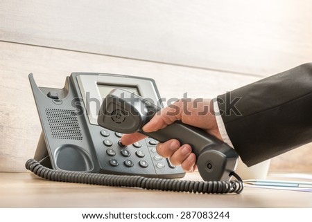 Closeup of a hand in a formal elegant suit dialing a telephone number on a classical black landline phone. Conceptual of global business communication and telemarketing.
