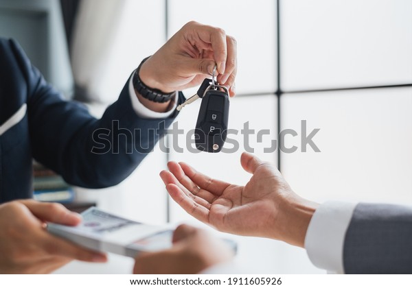 Closeup hand giving a car key and\
money for loan credit financial, lease and rental\
concept