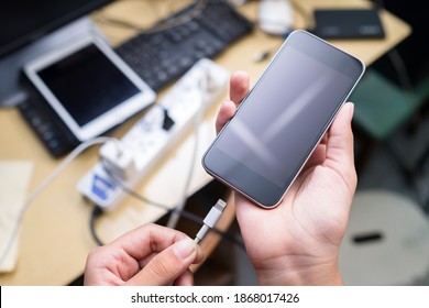 Closeup Hand Going To Charge Battery On Mobile Phone With Many Messy Electronic Multiple Sockets And Computer Device On The Desk