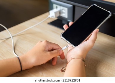 Closeup hand going to charge mobile phone battery from the built-in power socket on the table