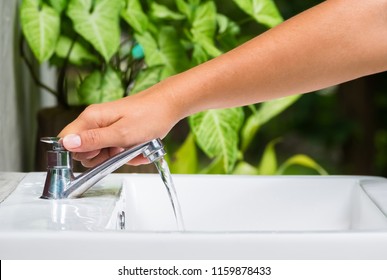 Closeup Hand Going To Turn Off The Tap On Washing Basin With Green Plant On Background