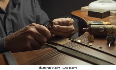 Close-up of a hand of a goldsmith polishing a precious jewel with shiny diamonds. To make the jewel it takes: precision, craftsmanship and patience. Concept of gold, luxury.
