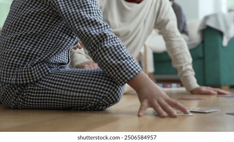 Close-up of a child’s hand and grandfather's hand while playing a matching game on the floor, focus on hands and game pieces, intergenerational bonding, family interaction, fun indoor activity - Powered by Shutterstock