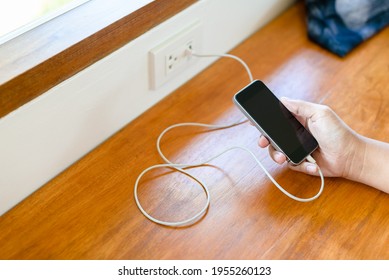 Closeup Hand Hold The Smart Phone While Charging Battery By Usb Power Socket On The Wall