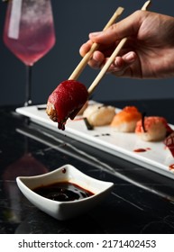 Close-up Hand Holding Bamboo Chopsticks A Piece Of Sushi While Soaking It In Soy Sauce At Restaurant. Front View. Japanese Cuisine Concept.