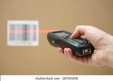 closeup of hand holding bar code scanner and scanning code on cardboard box