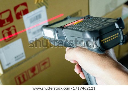 closeup hand holding bar code scanner scanning red laser with shipment on label of product, warehouse inventory management.