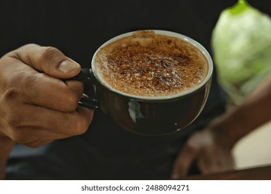 Close-up of a hand holding a creamy, perfectly caramelized crème brûlée coffee in a black cup. Ideal for promoting gourmet coffee, café menus, food blogs, and lifestyle content focusing on coffee  - Powered by Shutterstock