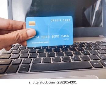 A close-up of a hand holding a credit card in front of a laptop, symbolizing online shopping and digital payment methods in modern finance.

