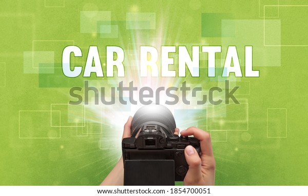 Close-up of a hand holding digital\
camera with CAR RENTAL inscription, traveling\
concept