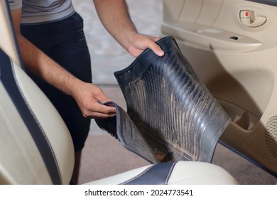 Close-up Of A Hand Holding A Dirty Black Rubber Car Floor Mat With Accelerator And Brake Inside The Cabin Before Dusting, Vacuuming, Dry Cleaning, Washing The Car.