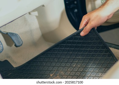 Close-up Of A Hand Holding A Dirty Black Rubber Car Floor Mat With Accelerator And Brake Inside The Cabin Before Dusting, Vacuuming, Dry Cleaning, Washing The Car.