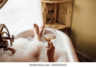 Close-up of a hand holding an elegant glass of champagne in the bathroom. A young woman takes a bubble bath and drinks sparkling wine. Vintage retro interior. Relaxation, rest and weekend concept. - Powered by Shutterstock