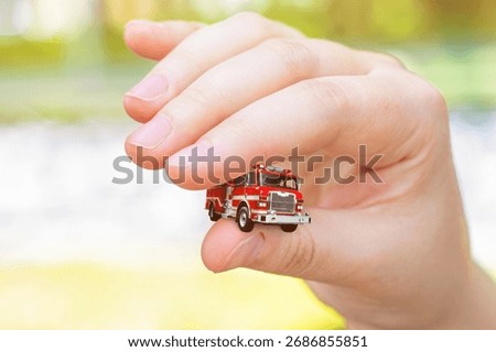 Close-up of a hand holding a fire engine. Background on the topic of insufficient fire safety. Poor provision of fire protection and municipal services.