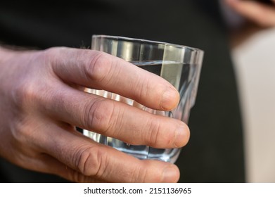 A Close-up Of A Hand Holding A Glass Of Water. A Mature Man In A Black Shirt Holds A Glass Of Clear Drinking Water In His Hand.
