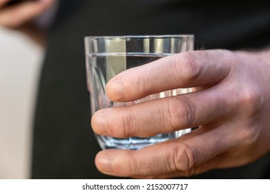 A Close-up Of A Hand Holding A Glass Of Water. A Mature Man In A Black Shirt Holds A Glass Of Clear Drinking Water In His Hand.