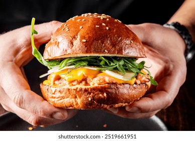 A close-up of a hand holding a gourmet burger with fresh greens, melted cheese, and a juicy patty on a sesame bun. Perfect for food blogs, restaurant menus, or culinary magazines. - Powered by Shutterstock