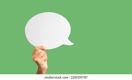 Close-up of hand holding a green speech bubble against a green background in the studio. Close-up photo. Space for text - Shutterstock ID 2209299787