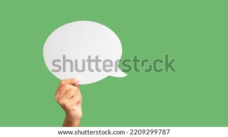 Close-up of hand holding a green speech bubble against a green background in the studio. Close-up photo. Space for text