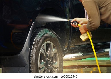 Closeup hand holding high-pressure water hose a man in car care spraying into wheel and tire until water droplets sprayed to cleaning for car washing services.