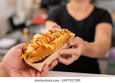 Close-up of a hand holding a hot dog with mustard and ketchup, with an out-of-focus person in the background. Perfect for themes of street food, casual dining, and food presentation. - Powered by Shutterstock