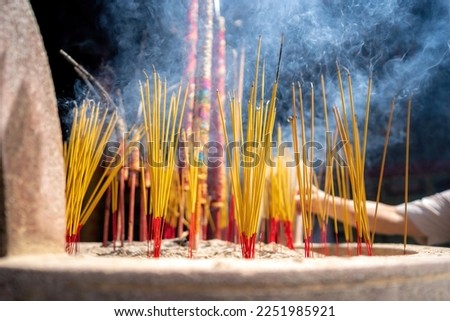close-up of a hand holding incense. The background is an unspecified, faded temple. Concept of spiritual and religious