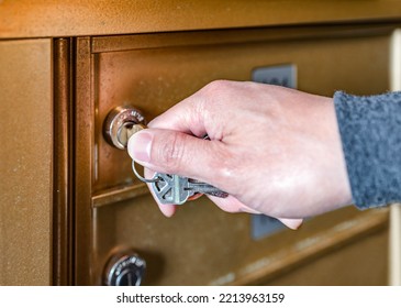 Closeup Person’s Hand Holding Key Unlock-lock Mailbox, Selective Focus. Receiver Get Mail From Metal Copper Color Storage In The Mail Room, Depth Of Field. Residential Indoor Letterbox.