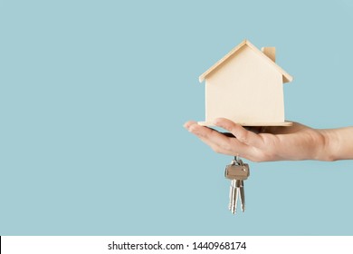 Close-up of hand holding keys and wooden house model against blue background