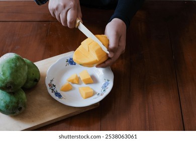 Closeup of a hand holding a knife and cutting the fresh ripe Indonesian mango to white plate, one of the most popular tropical fruits, Fresh fruit. Tropical fruit. - Powered by Shutterstock