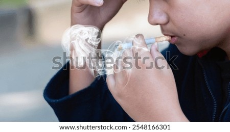 Closeup hand holding lighted cigarrette of asian smoking boy in private area of school and house to avoid punishment from teachers or parents, new edited.