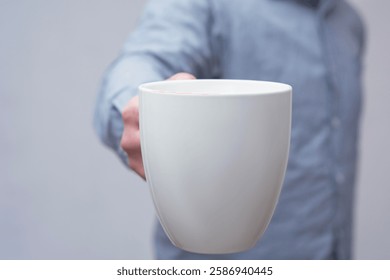 Closeup of a hand holding a mockup of a large white mug on a light background. Concept for use in logo in branding