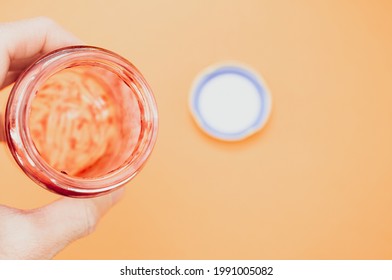 A Closeup Of A Hand Holding An Open Empty Strawberry Jam Jar Isolated On Light Orange Background