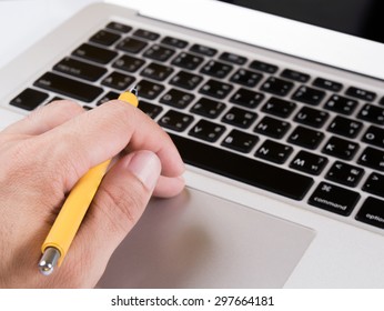 Close-up of hand holding pen while working over laptop