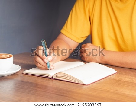 Close-up of hand holding a pen writing on a notebook on the desk. Space for text. Concept note taking or writing reports